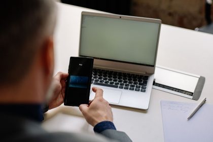 Profissional usa o celular para realizar um pagamento digital ao lado de um laptop em um escritório