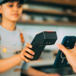Caixa realiza um pagamento por aproximação com smartphone e leitor de cartões em uma loja