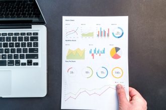 Documentos com gráficos e tabelas ao lado de um computador portátil, representando análise de dados financeiros.