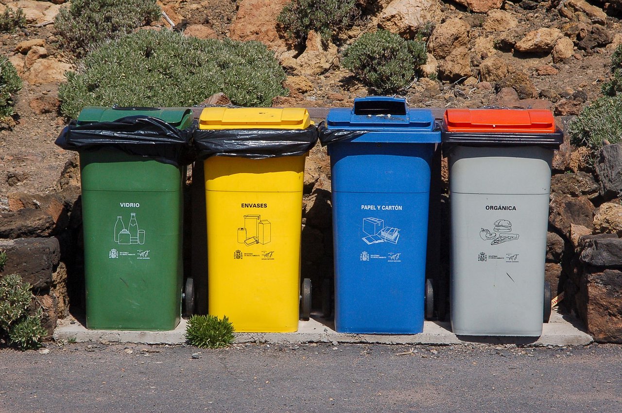 Quatro contentores para separação de vidro, embalagens, papel e resíduos orgânicos instalados ao ar livre.