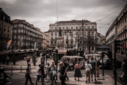 Zona pedonal movimentada na Praça do Rossio, em Lisboa, com pessoas a circular diante de edifícios históricos.