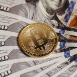 Moeda de bitcoin sobre notas de dólar, simbolizando a ligação entre activos digitais e o sistema financeiro tradicional.