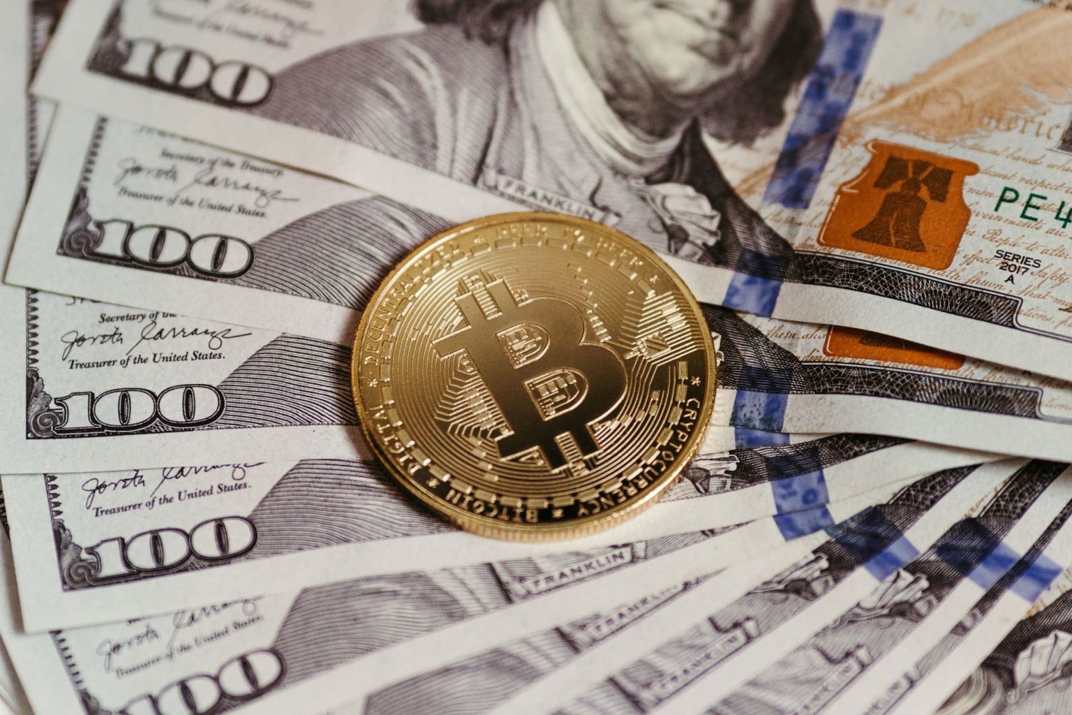 Moeda de bitcoin sobre notas de dólar, simbolizando a ligação entre activos digitais e o sistema financeiro tradicional.