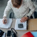 Homem analisa documentos financeiros ao lado de uma calculadora sobre a mesa, em um escritório.