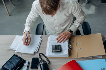 Homem analisa documentos financeiros ao lado de uma calculadora sobre a mesa, em um escritório.